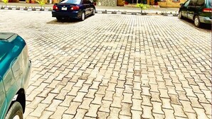 Um edifício com vários andares, uma entrada central, área de estacionamento e veículos.