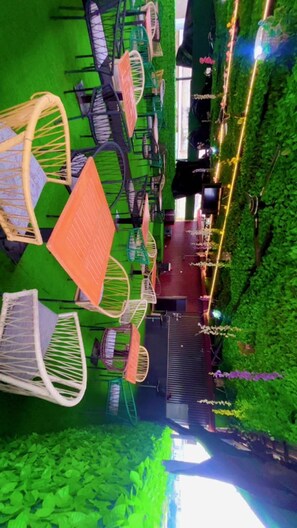 A row of outdoor seating with chairs and tables, surrounded by greenery and a pathway. - Centenary Hotel (Abuja)