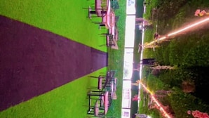 Área de refeições ao ar livre com mesas e cadeiras, cercada por vegetação e luzes decorativas.