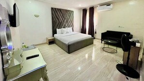 Quarto de hotel com cama, escrivaninha, cadeira, televisão e ar condicionado.
