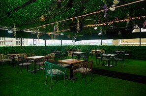 An indoor dining area with tables and chairs, a green artificial grass floor, and hanging plants. - Centenary Hotel (Abuja)