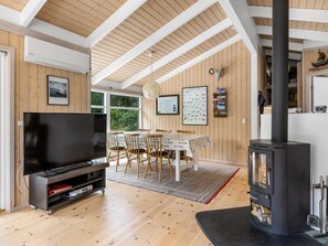 Ein modernes Wohnzimmer mit Flachbildfernseher, Holzboden, einem Essbereich mit Tisch und Stühlen sowie einem Kaminofen.