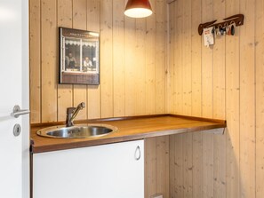 A kitchen with a wooden countertop, stainless steel sink, and a hanging light fixture.