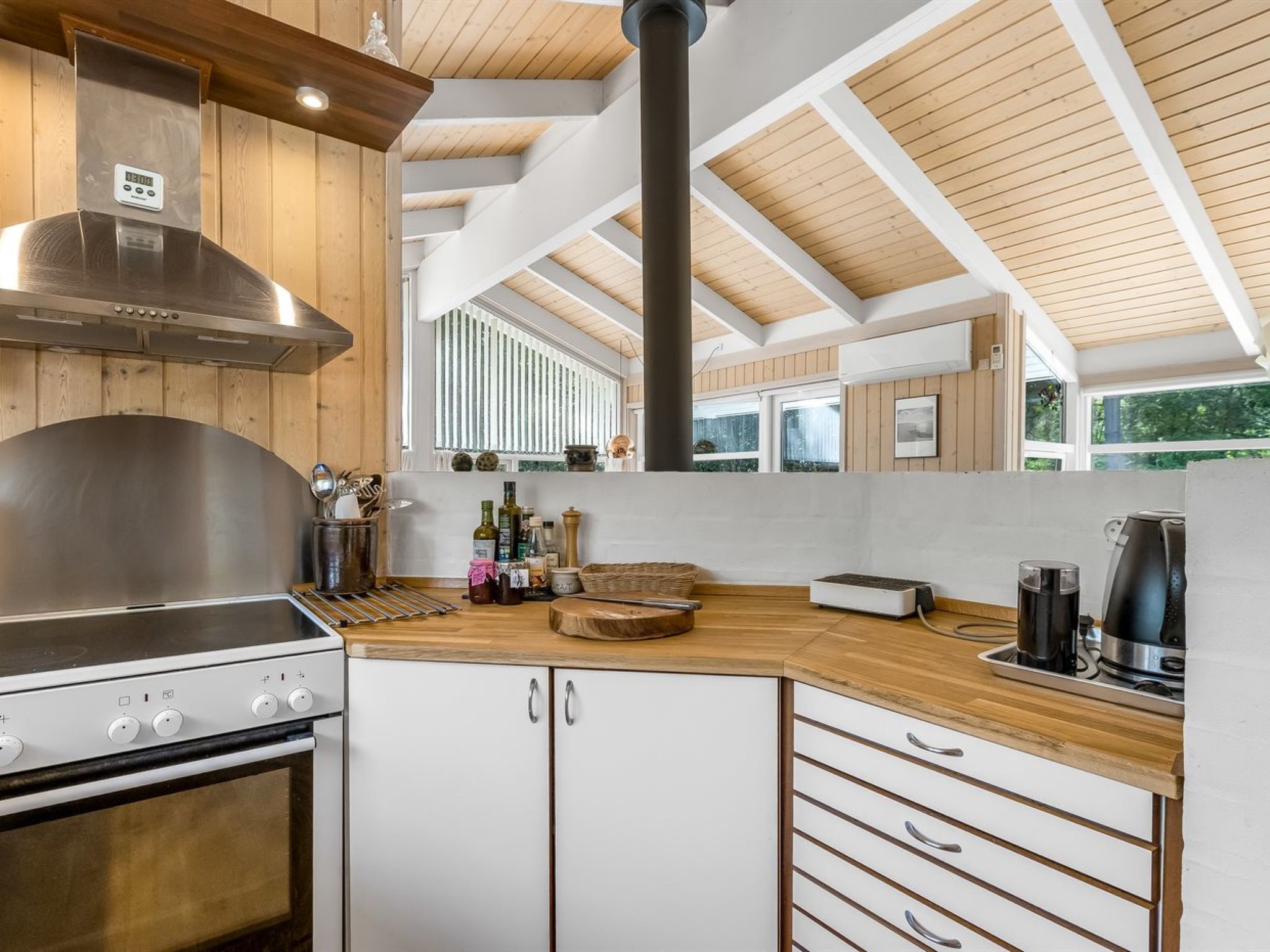 A modern kitchen with a stainless steel range hood, wooden cabinets, and a large window providing natural light.