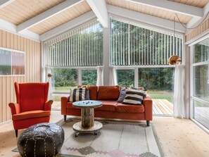 A conservatory with a wooden ceiling, a red sofa, a round coffee table, and a leather ottoman.