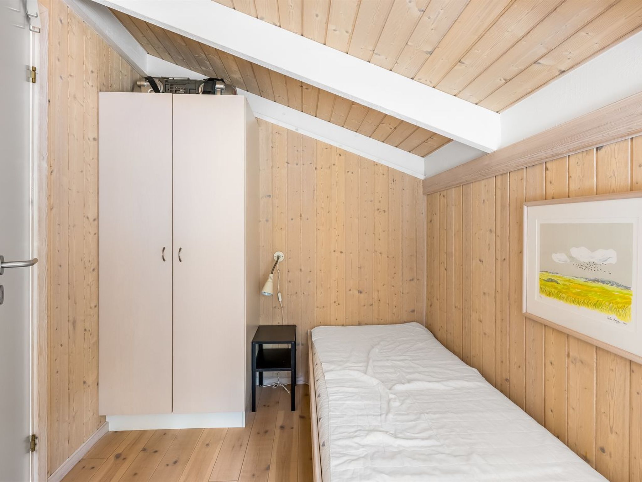 Een slaapkamer met een bed, een kledingkast, een bureau en een lamp.
