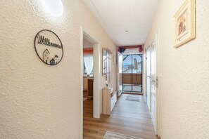 A hallway with a welcome sign, wooden flooring, and a view of the outside.
