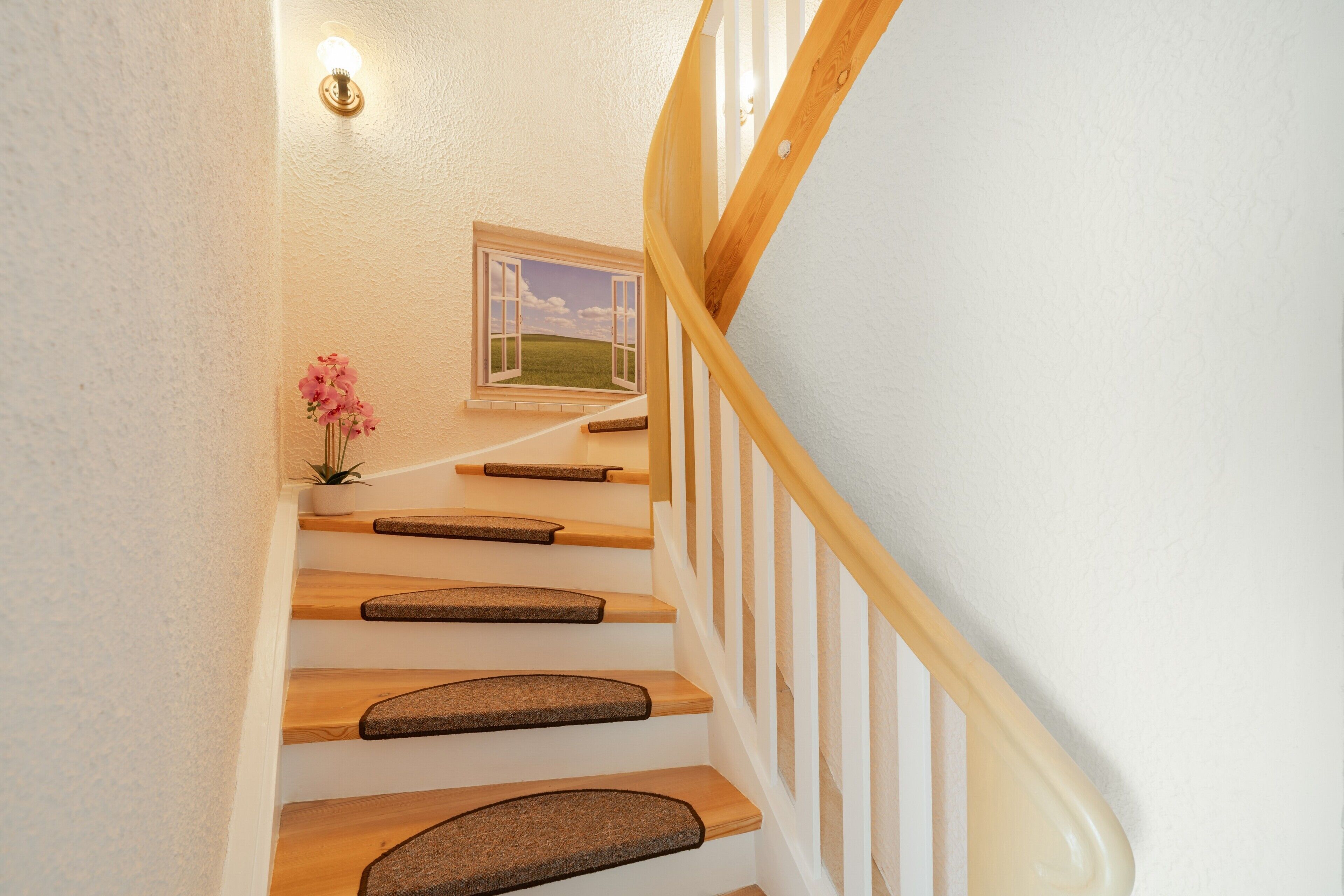 Eine Treppe mit Holzdielen und Geländer, die zu einer Fläche mit einem gerahmten Bild und einem Blumentopf führt.