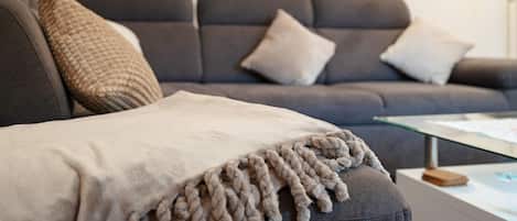 A grey sofa with a beige throw blanket and two cushions.