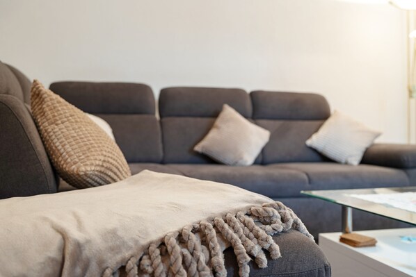 A grey sofa with a beige throw blanket and two cushions.