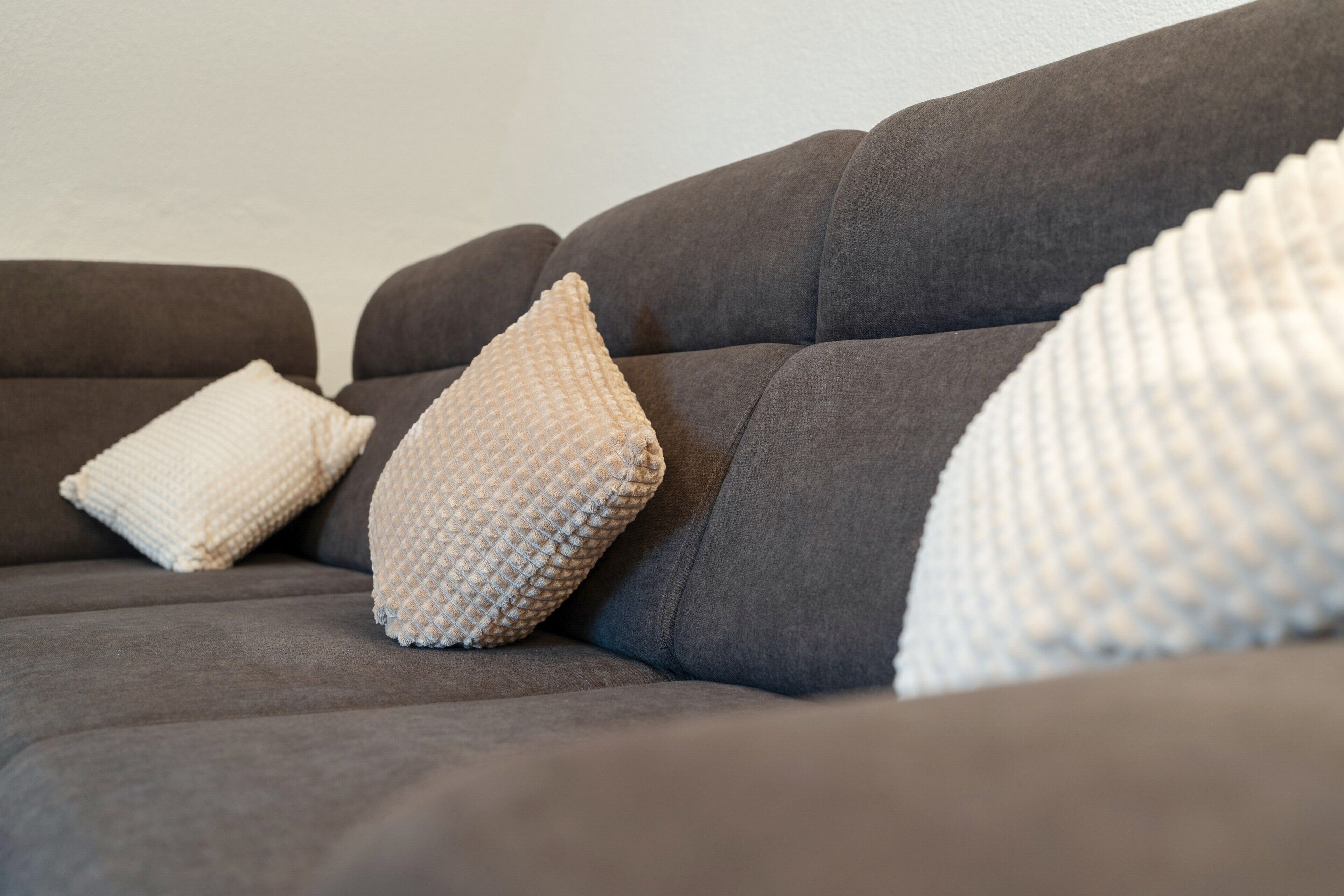 Un canapé gris avec trois coussins à texture variée.