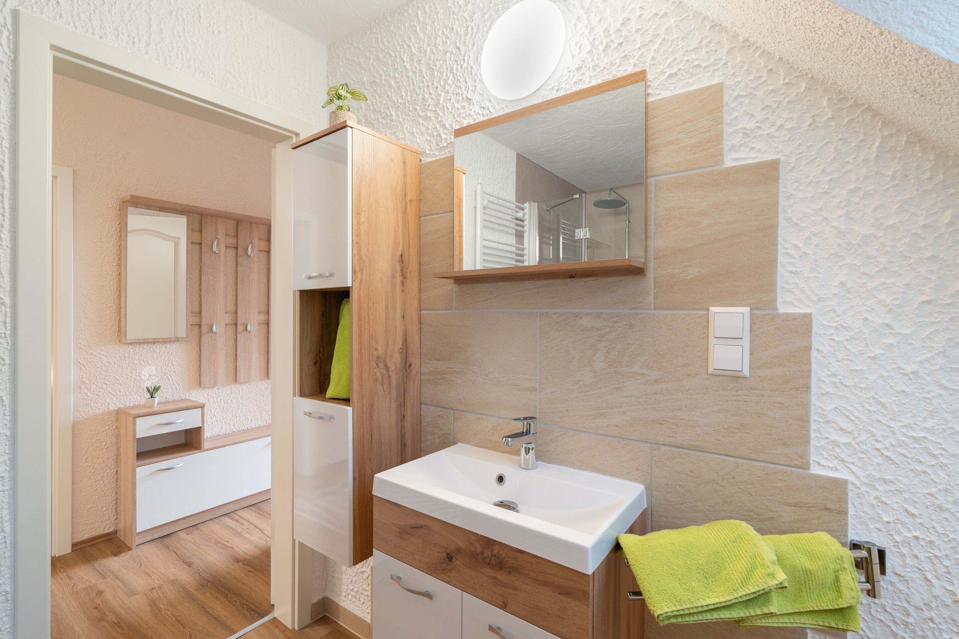 A modern bathroom with a white sink, wooden vanity, and a shower area.