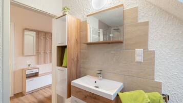 A modern bathroom with a white sink, wooden vanity, and a shower area.