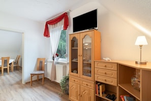 A room with a dining area, a television mounted on the wall, a cabinet with glass doors, and a lamp on a side table. - Apartment 'Ferienwohnung Am Hasepäddel' with Balcony and Wi-Fi (Fischbach bei Dahn)