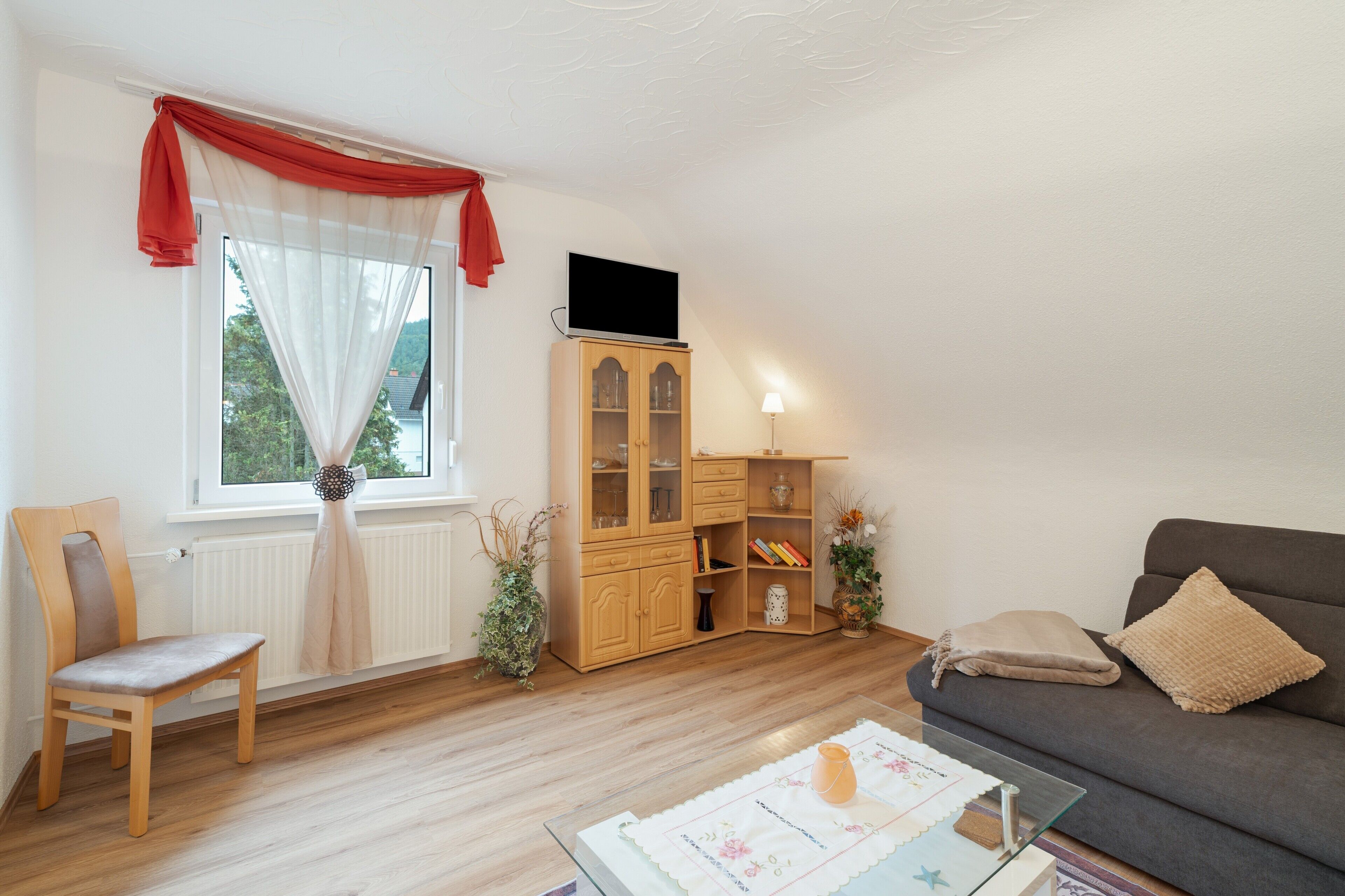 A living room with a wooden cabinet, a sofa, a chair, a TV, and a window with curtains.