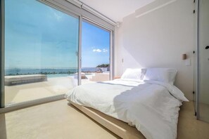 Ein Schlafzimmer mit einem großen Schiebeglasfenster, das auf einen Balkon mit Blick auf den Strand führt.