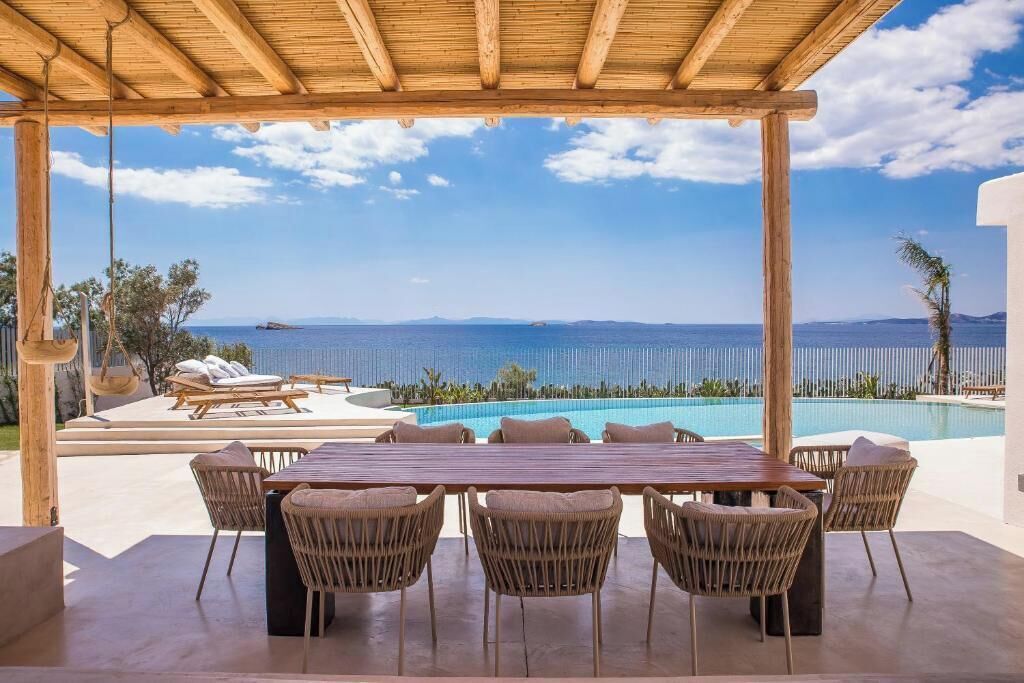 A covered outdoor area with a pool, lounge chairs, and a wooden table with chairs.