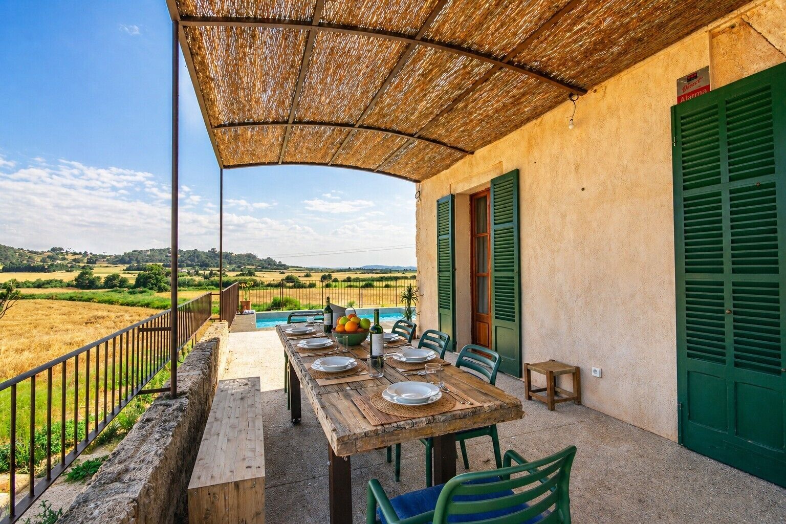 An outdoor dining area with a table set for four, a pool in the background, and a view of the countryside.