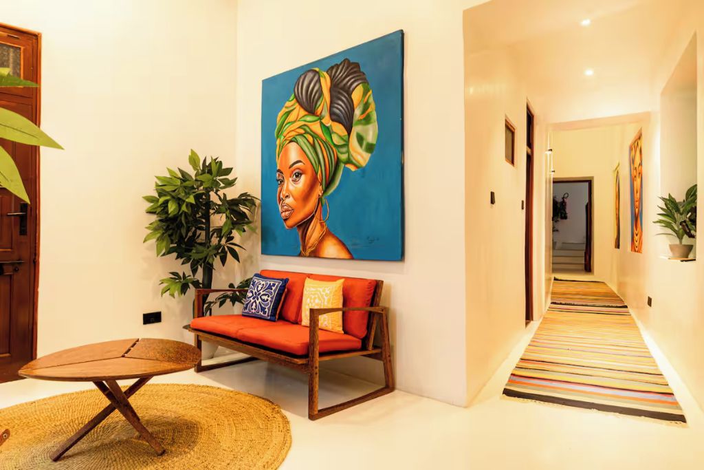 A hallway with a sofa, a painting, and a plant.
