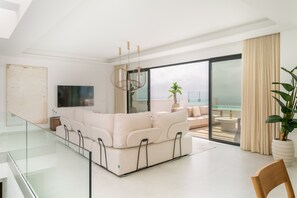 A modern living room with a large sofa, a flat-screen TV, and a balcony with a view of the sea. - Moana 4 - Luxury Home with Private Pool (Benalmádena)