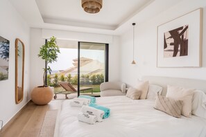 A modern bedroom with a large bed, a potted plant, a chair, and a view of the outdoors. - Moana 4 - Luxury Home with Private Pool (Benalmádena)