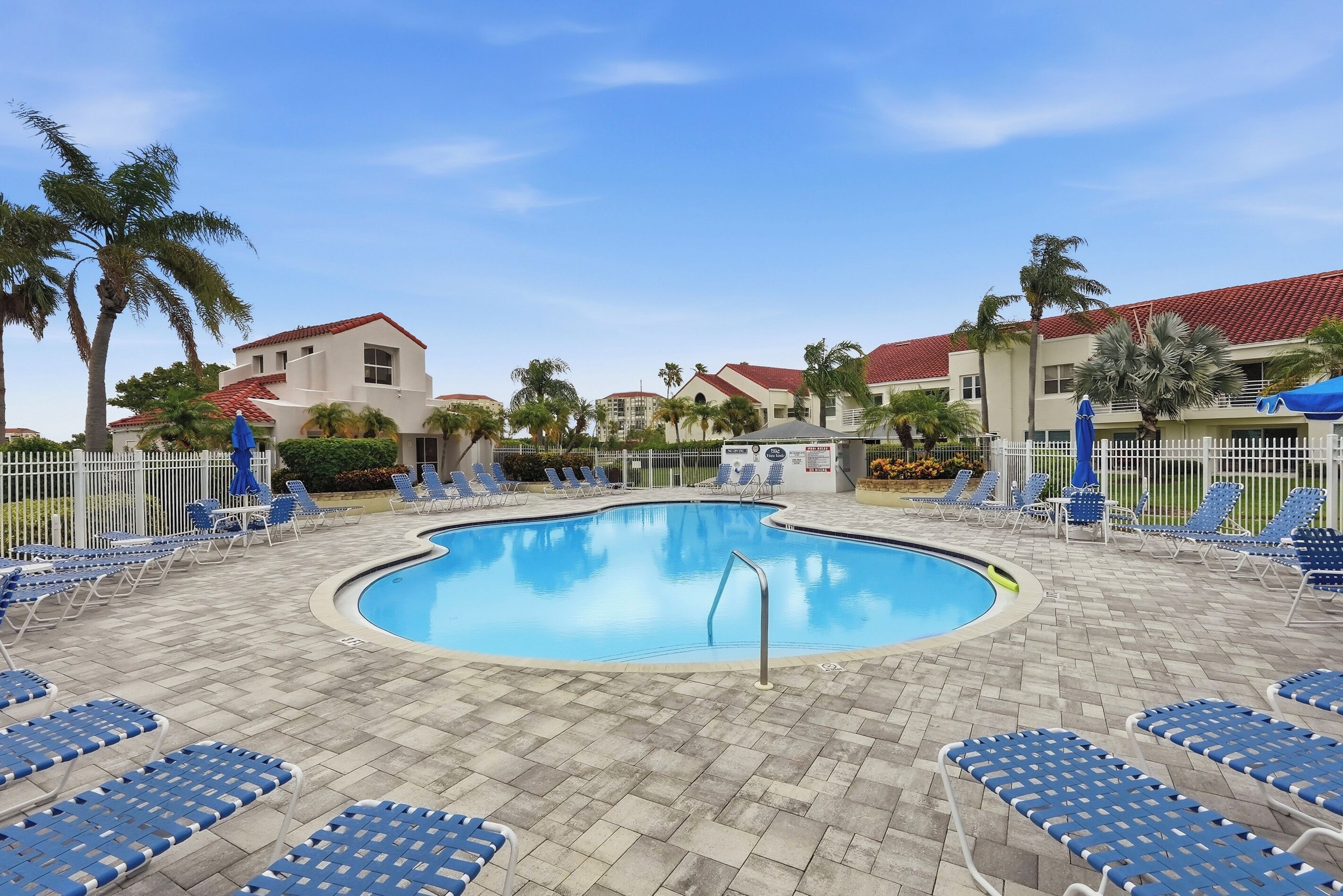 A swimming pool with blue lounge chairs and palm trees.