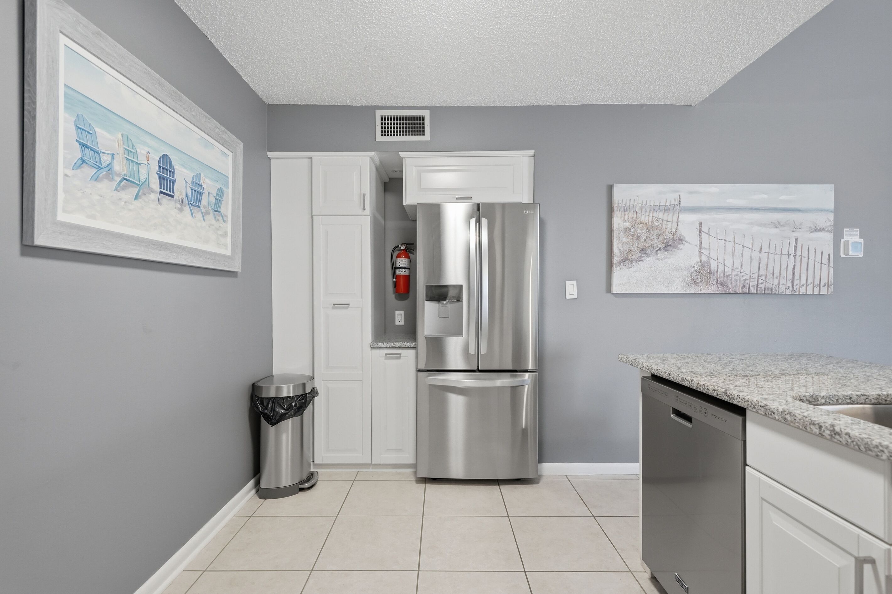 Una cocina moderna con un refrigerador de acero inoxidable, armarios blancos y piso de baldosas.