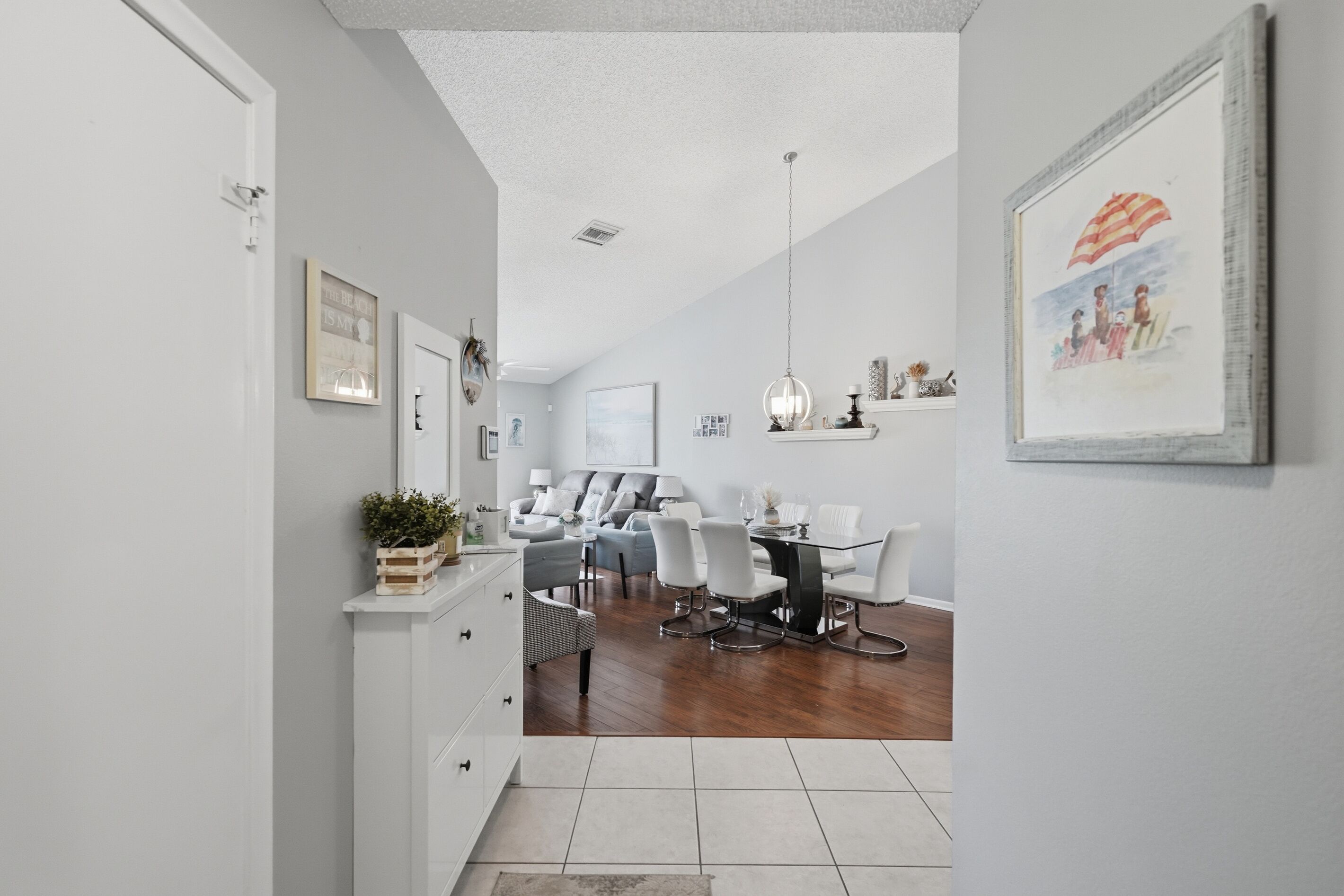 A modern dining area with a glass table and white chairs, a white sofa, and a ceiling light.