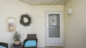 Eine überdachte Veranda mit zwei Korbstühlen, einer Tür, einem Kranz und einem Feuerlöscher.