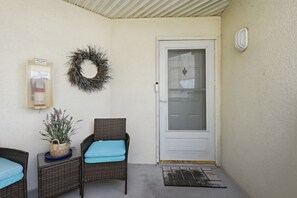 En inglasad veranda med två fåtöljer i rotting, en dörr, en krans och en brandsläckare.