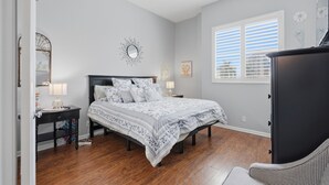 A bedroom with a bed, a nightstand, a dresser, a window with blinds, and a ceiling fan.