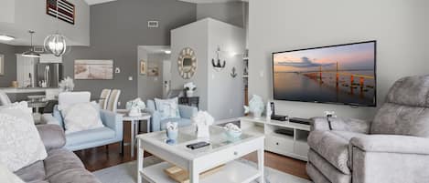 Una sala de estar moderna con un televisor de pantalla plana, sofás grises, una mesa de centro y vista a un puente.