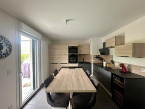 Una cuina moderna amb taula i caires de fusta, forn de mur i taulell negre.