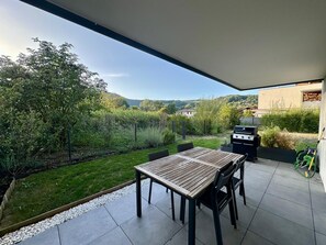 Une terrasse extérieure avec une table et des chaises, un barbecue et une vue sur un paysage verdoyant avec des collines.