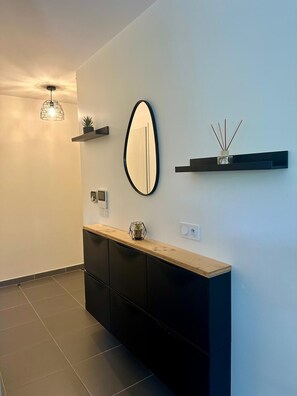 A modern bathroom with a vanity, a mirror, a light fixture, and a wall-mounted shelf with a diffuser.