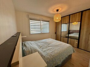 Une chambre à coucher comprenant un lit, une commode, une fenêtre avec des stores et un luminaire suspendu.