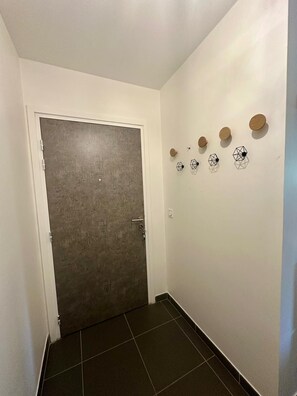 Un couloir avec une porte fermée, un sol carrelé et des objets décoratifs fixés au mur.