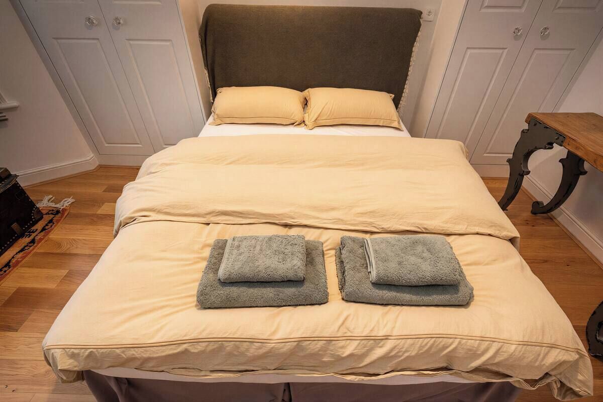 A bed with a beige bedspread, two pillows, and two folded towels.