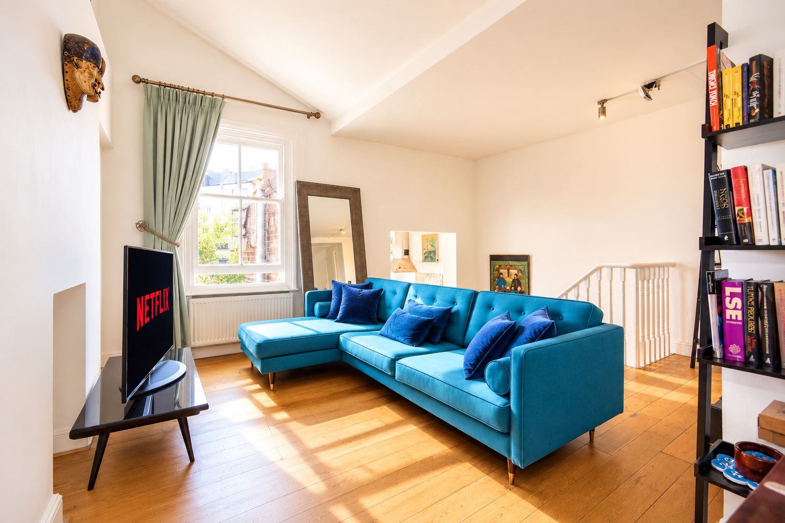 A living room with a blue sofa, a television, a bookshelf, and a window with curtains.