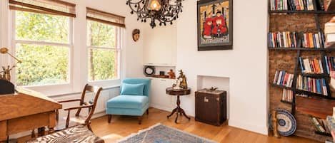 A room with a blue armchair, wooden floor, a patterned rug, a bookshelf, and a wall-mounted painting.