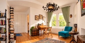 A cozy room with a wooden desk, a blue armchair, and a bookshelf filled with books. - 2-Bed Chelsea Flat | Balcony & River View (London)