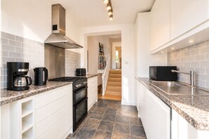 A modern kitchen with white cabinetry, a gas stove, a coffee maker, and a microwave. - 2-Bed Chelsea Flat | Balcony & River View (London)