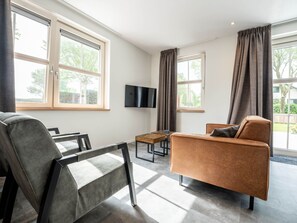 Ein modernes Wohnzimmer mit einer Couch, einem Sessel, einem Couchtisch und einem Flachbildfernseher.