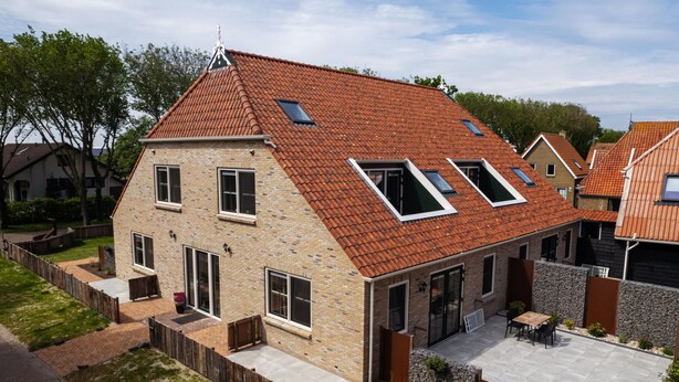 Une maison à deux étages, dotée d’un toit en pente, de lucarnes et d’une terrasse dallée.