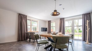 Une pièce spacieuse avec une grande table ronde, six chaises, un téléviseur à écran plat et de grandes fenêtres dotées de rideaux.