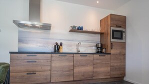 Une cuisine moderne avec des armoires en bois, une hotte de cuisinière en acier inoxydable, un four à micro-ondes encastré et un pare-feu orné d’un motif de carreaux bleu-gris.