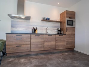 Eine moderne Küche mit Holzschränken, einer Edelstahl-Dunstabzugshaube, einer eingebauten Mikrowelle und einer Spritzschutzwand mit blau-grauem Muster.
