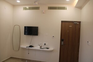 Habitació amb televisió penjada, una porta de fusta i una estant blanca amb dispositius electrònics.
