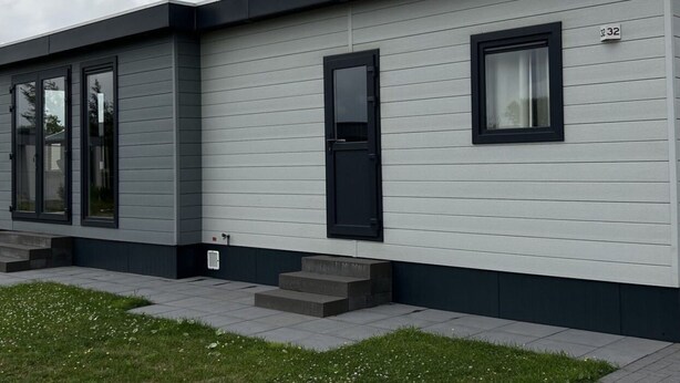 A modern building with a grey facade, a black door, and a window with a curtain. - Vakantiepark de Zeeuwse Parel - Noordzee Deluxe by Interhome (Scherpenisse)