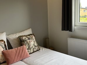 Ein Schlafzimmer mit Bett, Kissen, Heizkörper und einem Fenster mit Vorhängen.